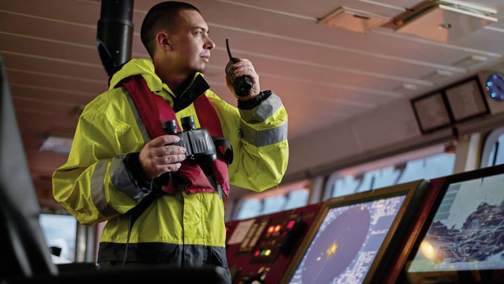 Pilot on the bridge of a vessel, operation radio and holding binoculars.